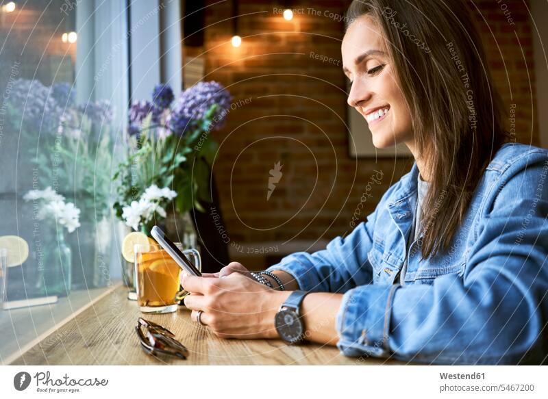 Smiling young woman using phone in cafe smiling smile mobile phone mobiles mobile phones Cellphone cell phone cell phones females women telephones communication