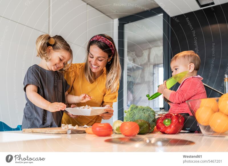 Smiling mother and girl preparing food while baby daughter sitting on kitchen island color image colour image indoors indoor shot indoor shots interior