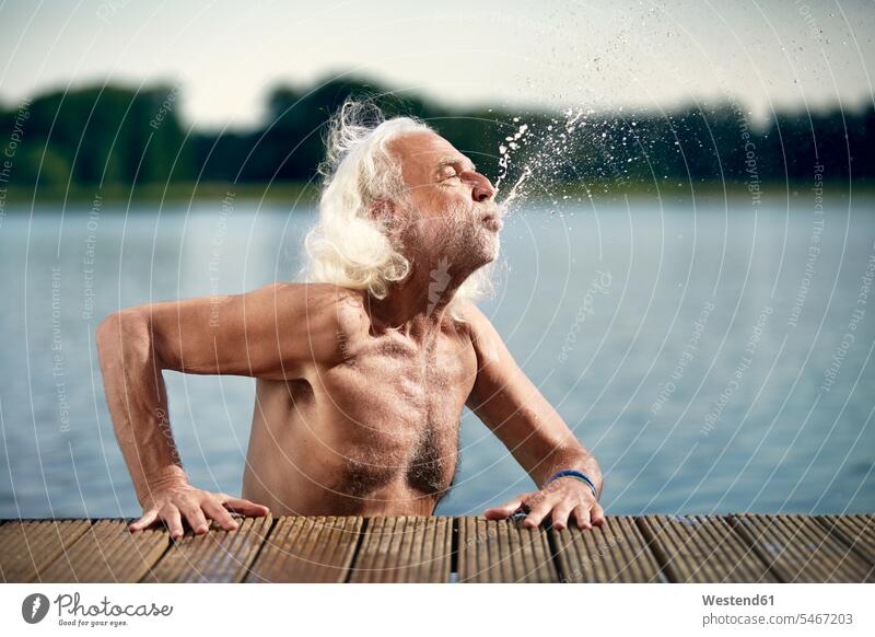 Senior man with white hair leaning on jetty splashing with water splash water splash of water lake lakes senior men senior man elder man elder men