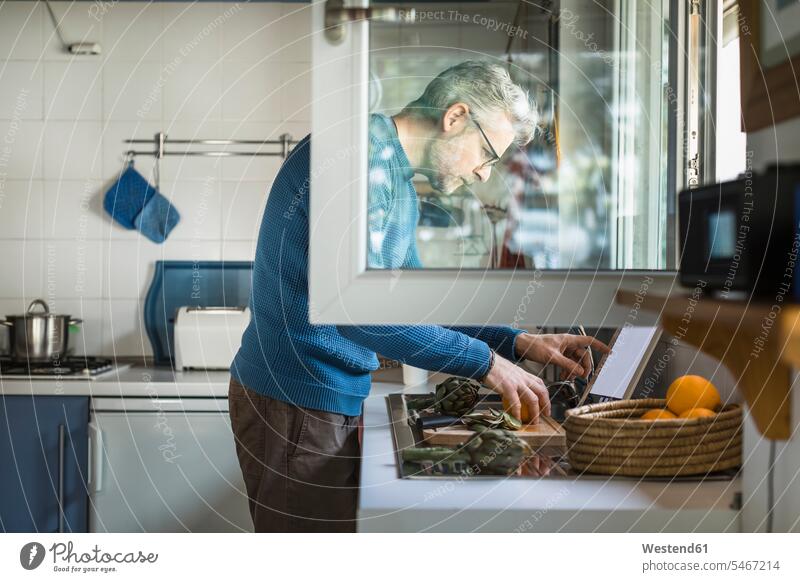 Mature man preparing artichoke in his kitchen using digital tablet human human being human beings humans person persons celibate celibates singles