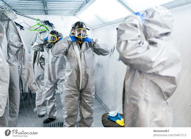 Team of sanitation workers wearing protective coveralls and gas masks while standing in locker room color image colour image Corona Virus Coronavirus disease