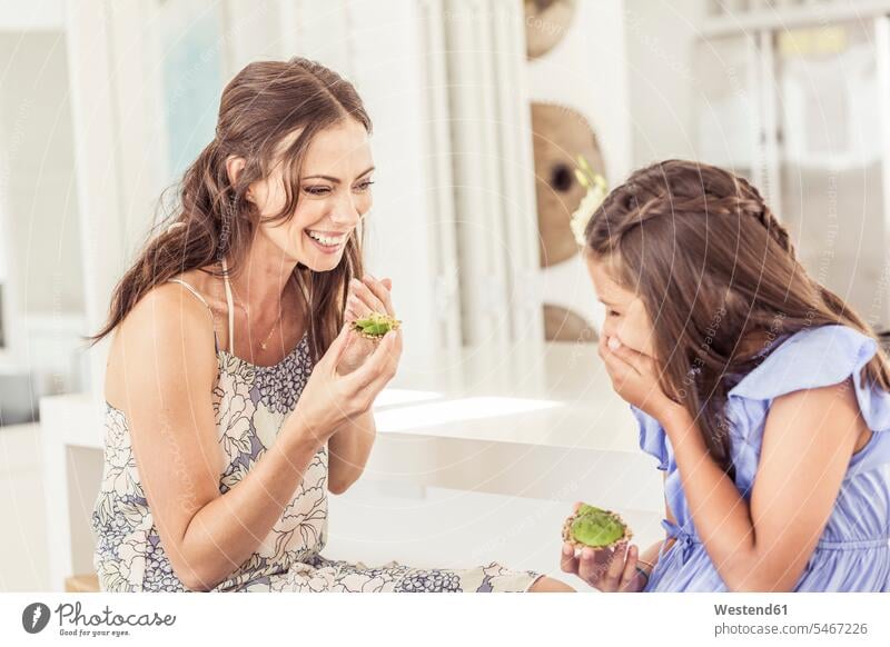 Happy mother and daughter eating avocado bread at home dresses smile delight enjoyment Pleasant pleasure Cheerfulness exhilaration gaiety gay glad Joyous merry