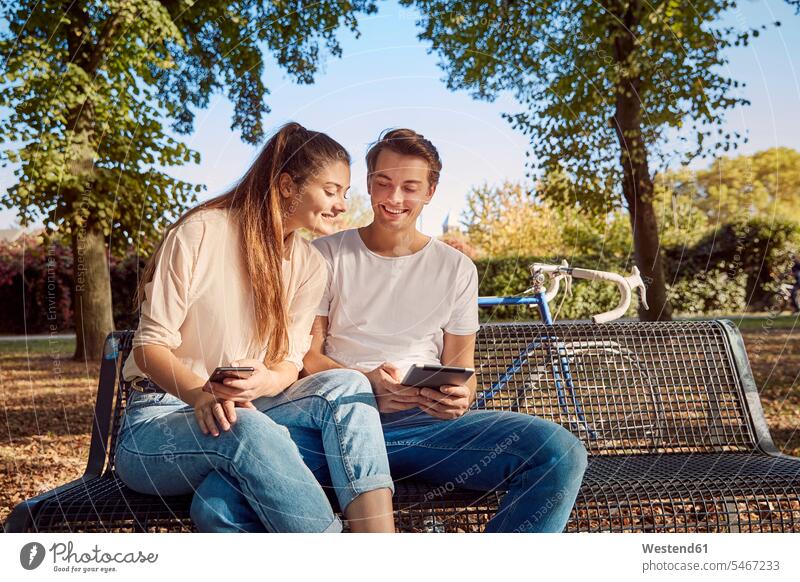 Young couple in park sitting on a bench with cell phone and tablet benches digitizer Tablet Computer Tablet PC Tablet Computers iPad Digital Tablet