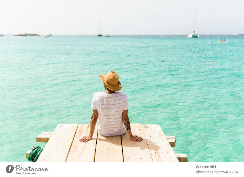 Back view of man sitting on wooden jetty looking at sea, Formentera, Spain human human being human beings humans person persons caucasian appearance