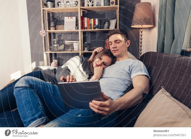 Young couple using tablet on couch at home relaxed relaxation twosomes partnership couples settee sofa sofas couches settees digitizer Tablet Computer Tablet PC
