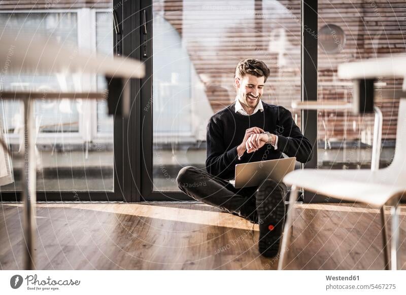 Businessman sitting on floor of his office, using laptop and smartwatch Seated sitting on ground Sitting On The Floor Sitting On Floor use on the phone call