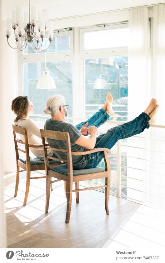 Relaxed mature couple sitting on chairs at home with feet up relaxed relaxation Seated twosomes partnership couples relaxing people persons human being humans
