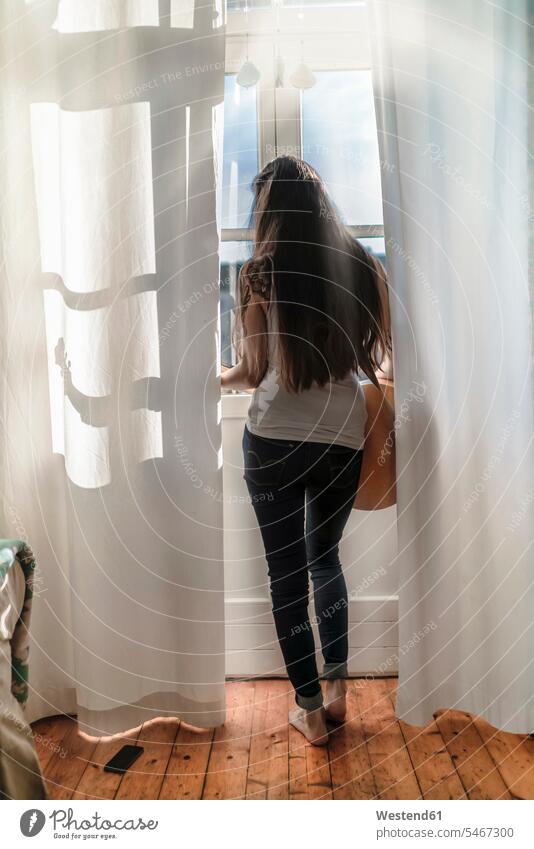 Rear view of a young woman standing at the window at home with a guitar human human being human beings humans person persons Mixed Race mixed race ethnicity