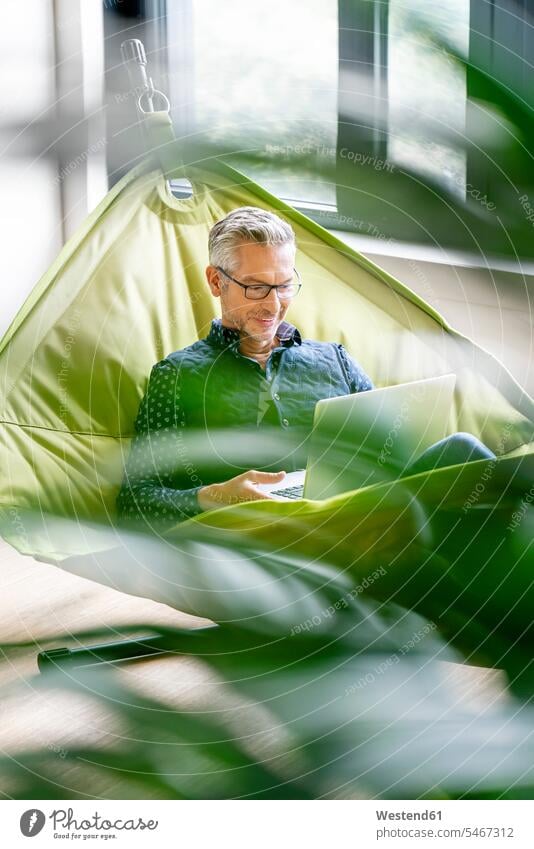 Smiling businessman sitting in hammock, using laptop human human being human beings humans person persons caucasian appearance caucasian ethnicity european 1
