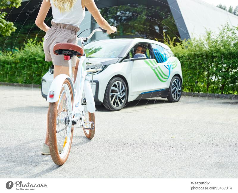 Woman with bicycle in front of electric car automobile Auto cars motorcars Automobiles bikes bicycles electric vehicle electric vehicles transportation