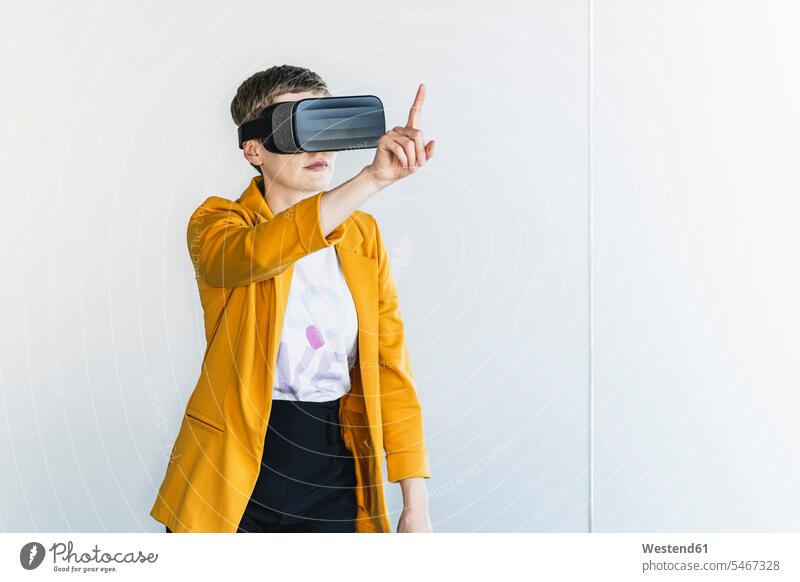 Businesswoman wearing blazer looking through virtual reality simulator while standing against wall in office color image colour image Germany indoors