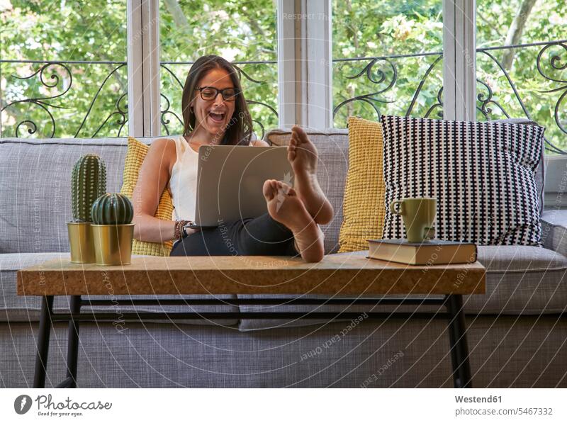 Cheerful woman using laptop while sitting on sofa in living room color image colour image indoors indoor shot indoor shots interior interior view Interiors day