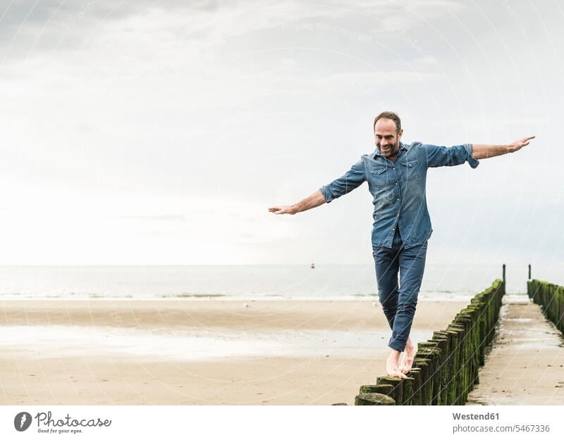 Carefree man with arms outstretched walking on wooden post at beach color image colour image Netherlands Holland The Netherlands Nederland leisure activity