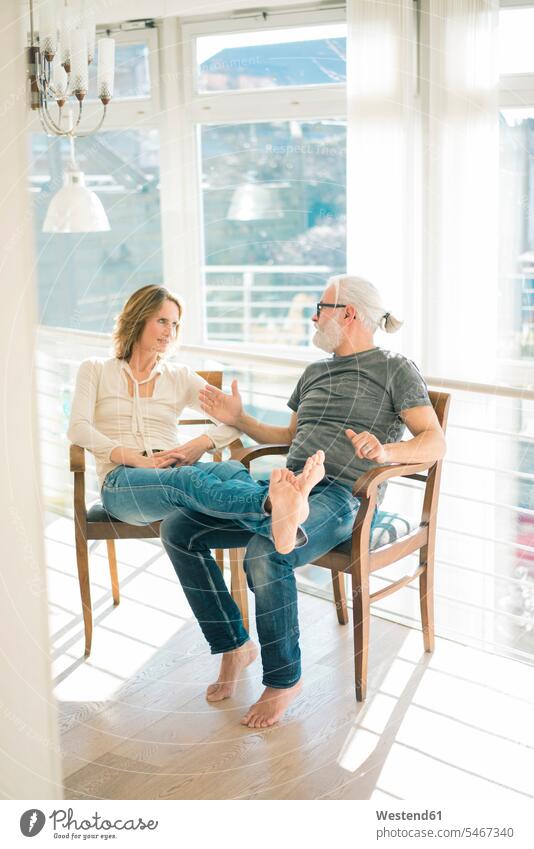 Relaxed mature couple talking on chairs at home relaxed relaxation speaking twosomes partnership couples sitting Seated relaxing people persons human being
