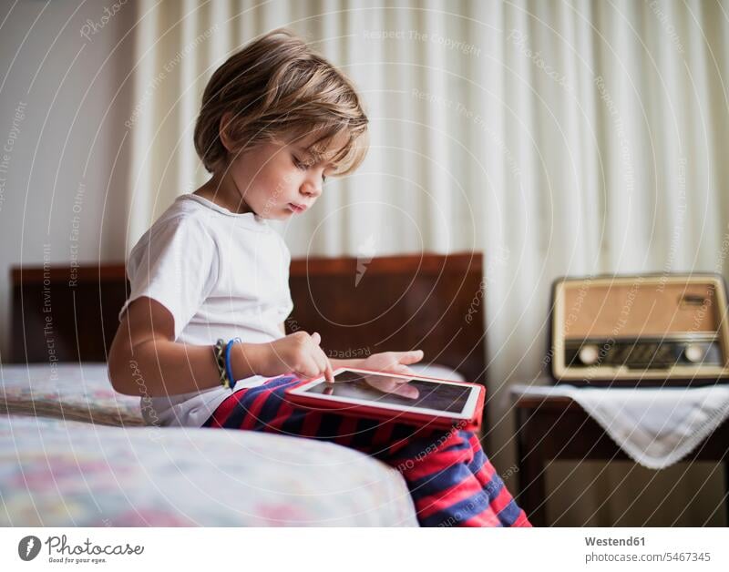Young boy sitting on bed using a tablet boys males digitizer Tablet Computer Tablet PC Tablet Computers iPad Digital Tablet digital tablets beds Seated child