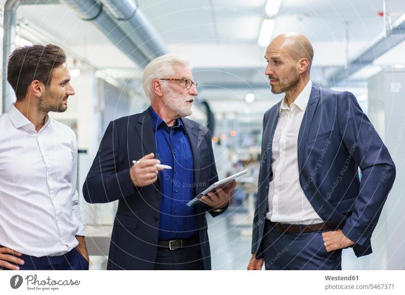 Senior male manager with colleagues discussing over digital tablet while standing at illuminated factory color image colour image indoors indoor shot