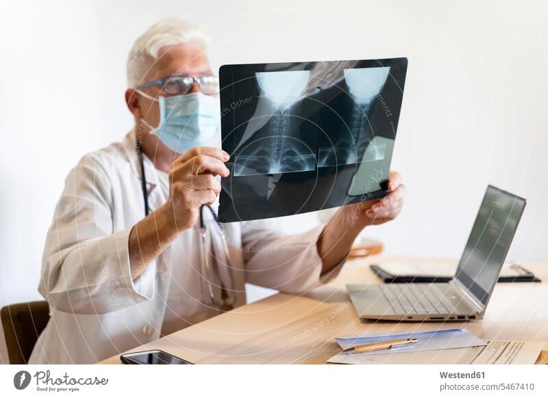 Doctor examining medical x-ray of human neck while sitting in clinic color image colour image indoors indoor shot indoor shots interior interior view Interiors