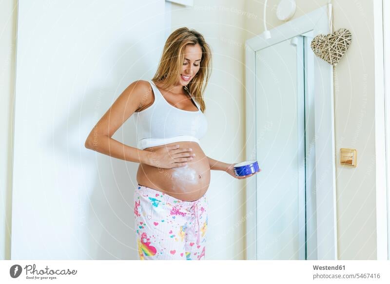 Pregnant woman putting cream on her belly applying creams cosmetic cream pregnant Pregnant Woman females women bellies stomach stomachs creaming Adults