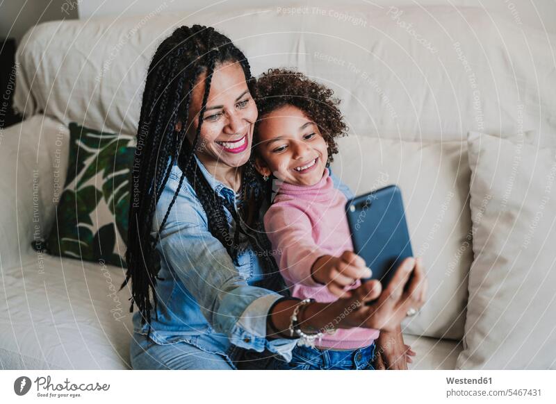 Portrait of happy mother and her little daughter taking selfie with smartphone on the couch couches settee settees sofa sofas cell phone cell phones Cellphone