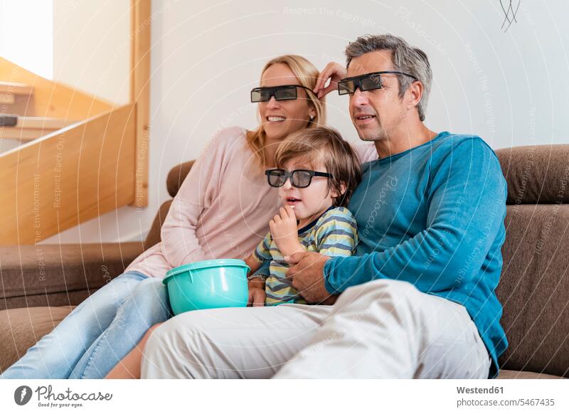 Father, mother and son wearing 3d glasses on couch at home watching Tv Bowls couches settee settees sofa sofas smile look seeing view viewing Seated sit relax