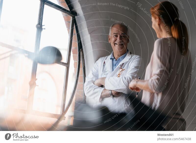 Smiling senior doctor talking to woman at the window in medical practice medical practices Doctors Office Doctor's Office senior men senior man elder man
