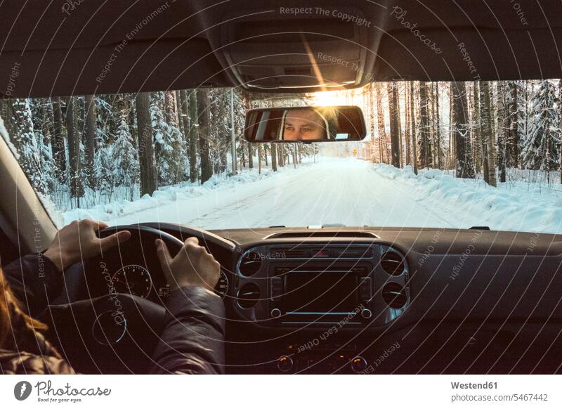 Finland, Kuopio, woman driving car in winter landscape at sunset Road Trip roadtrip Road-Trip Vehicle Interior Traveller Travellers Travelers Lens Flare