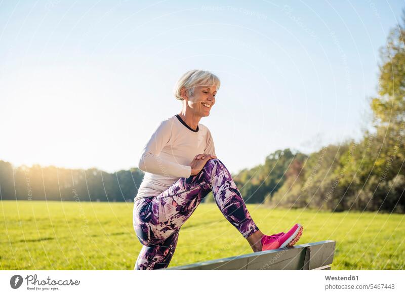 Smiling senior woman stretching on a bench in rural landscape benches country countryside smiling smile landscapes scenery terrain females women senior women