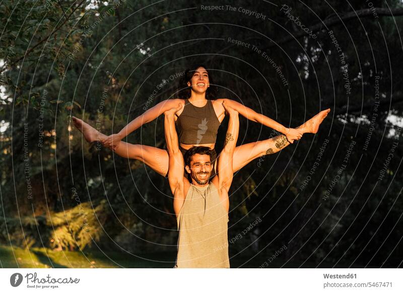 Smiling man lifting woman while practicing acroyoga in public park color image colour image Spain outdoors location shots outdoor shot outdoor shots