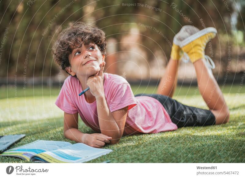 Boy lying in garden doing homework pupils schoolchild schoolchildren human human being human beings humans person persons curl curled curls curly hair books