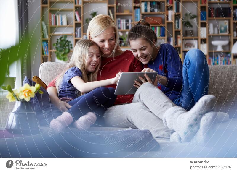 Mother and her daughters sitting on couch, having fun using digital laptop settee sofa sofas couches settees tablet digitizer Tablet Computer Tablet PC