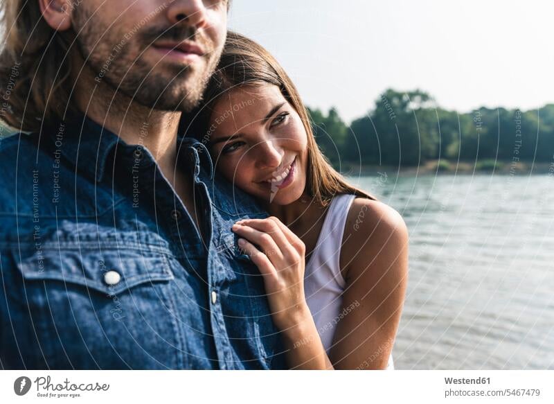 Smiling young woman leaning against man's shoulder at the riverside riverbank couple twosomes partnership couples River Rivers smiling smile water's edge