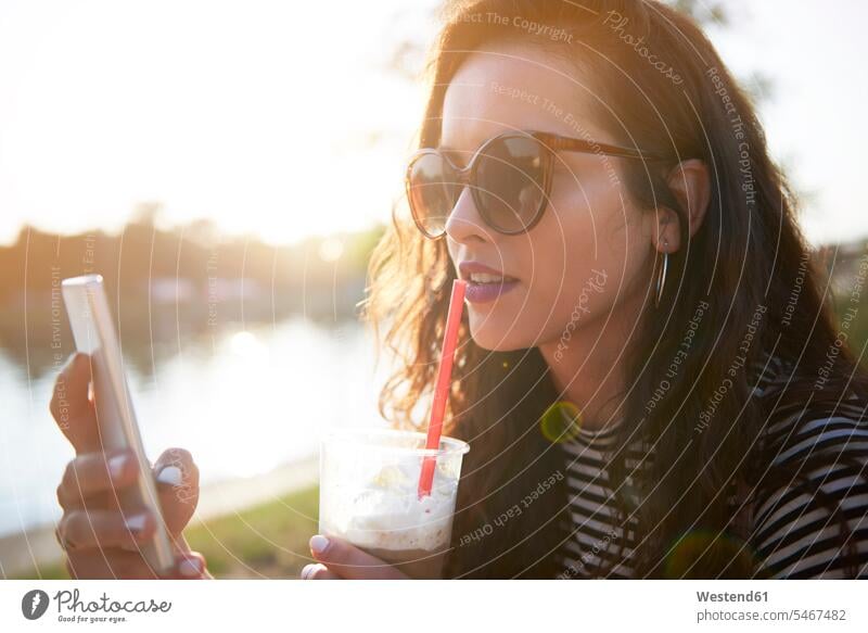 Stylish young woman with cell phone and takeaway drink outdoors at sunset Drink beverages Drinks Beverage mobile phone mobiles mobile phones Cellphone