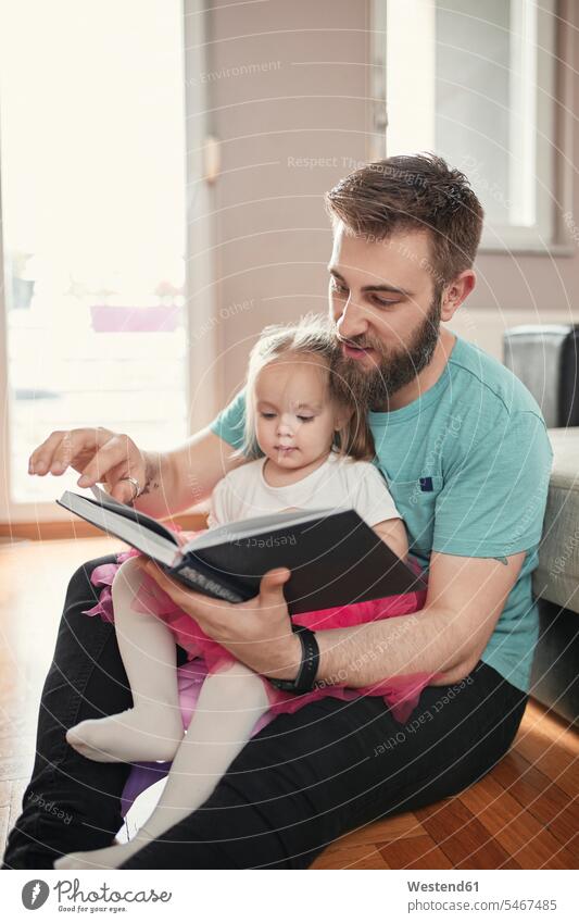 Father and daughter reading a book hear cuddle snuggle snuggling Seated sit play delight enjoyment Pleasant pleasure closeness propinquity at home free time