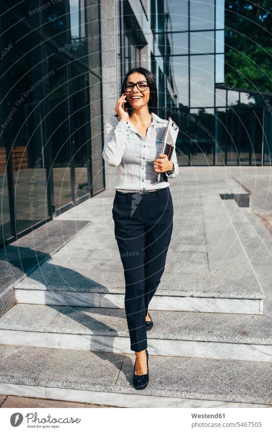 Smiling young businesswoman talking on cell phone outside office building human human being human beings humans person persons 1 one person only only one person