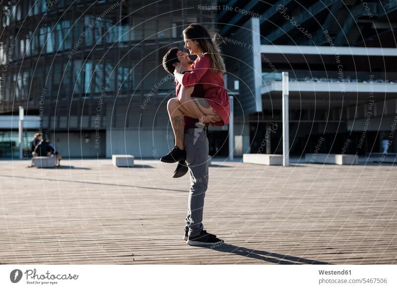 Young man lifting up happy girlfriend on city square lift up happiness plaza places Public Square couple twosomes partnership couples town cities towns people