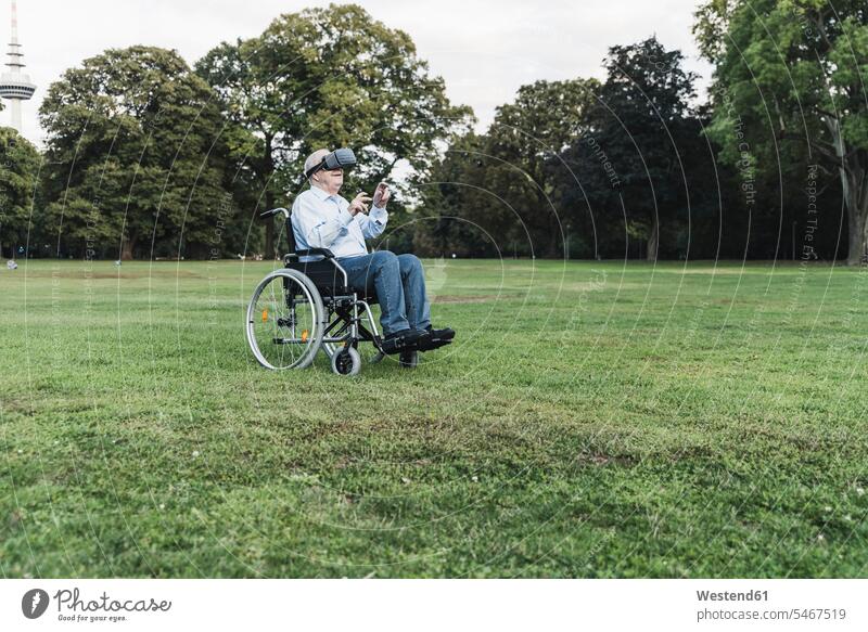 Senior man sitting in wheelchairin a park using Virtual Reality Glasses wheelchairs discover discovering relax relaxing smile look seeing view viewing Seated