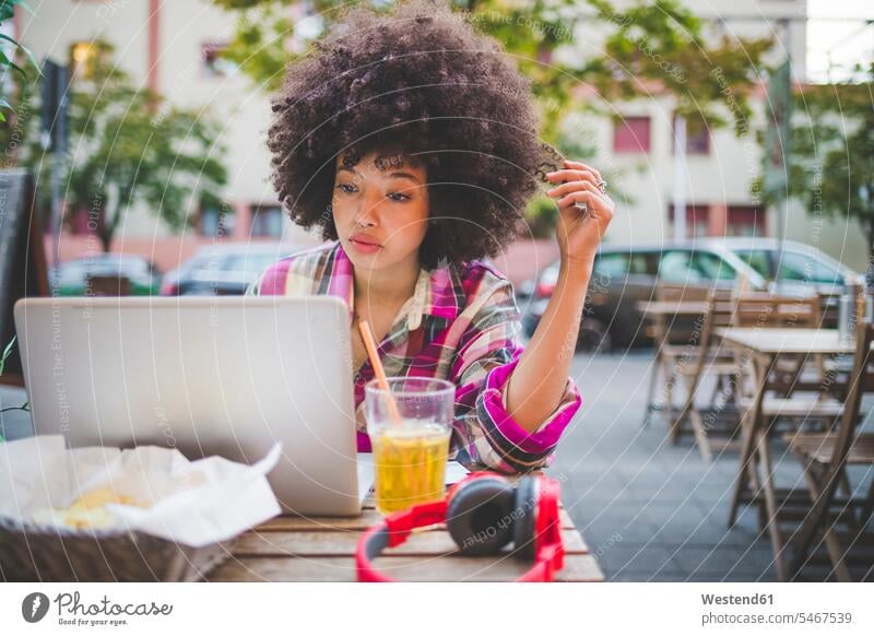 Young woman with afro hairdo using laptop at an outdoor cafe in the city human human being human beings humans person persons curl curled curls curly hair