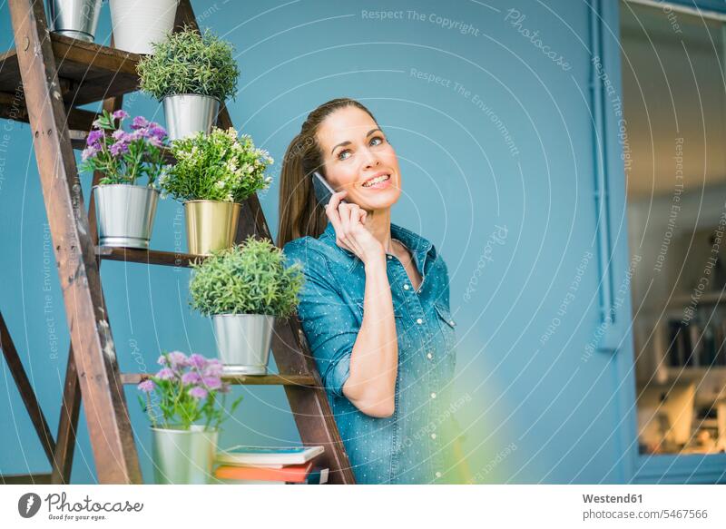 Beautiful woman in her home, decorated with plants, talking on the phone females women at home Smartphone iPhone Smartphones call telephoning On The Telephone