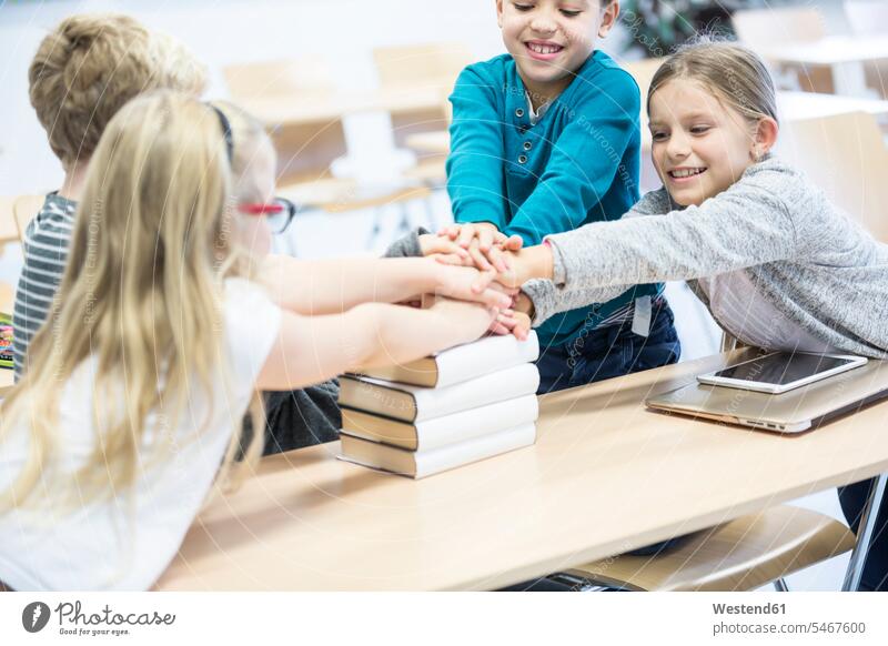 Happy pupils stacking hands on books in class happiness happy school schools piling pile human hand human hands Classroom class rooms Schoolroom classrooms