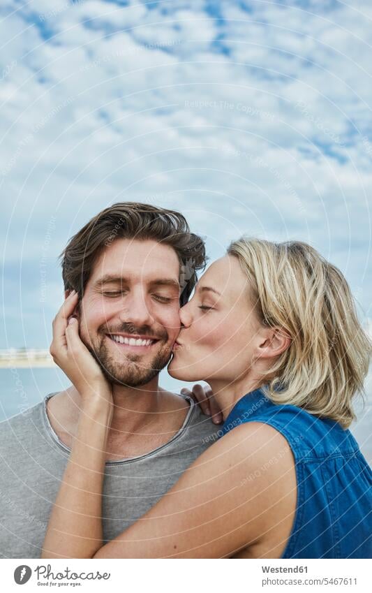 Happy young couple kissing on the beach happiness happy kisses hugging cuddling beaches twosomes partnership couples people persons human being humans