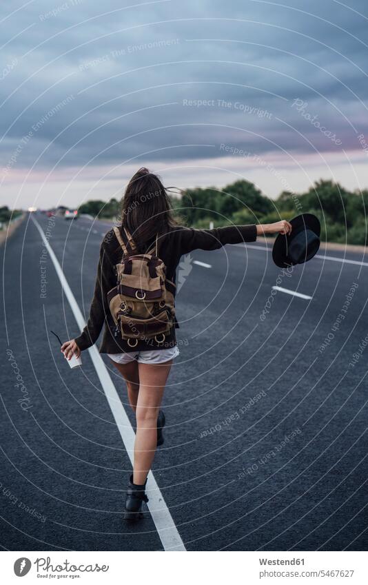 Back view of hitchhiking young woman with backpack and beverage standing at side line hitchhike hitch-hiking Drink beverages Drinks Beverage rucksacks backpacks
