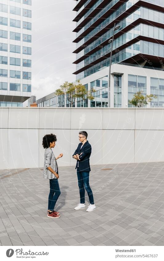 Two colleagues talking outside office building office buildings speaking built structure built structures face to face Facing Each Other looking at each other