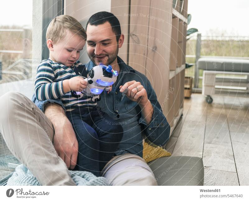 Father and son playing with a toy robot at home father pa fathers daddy dads papa sons manchild manchildren robots toys parents family families people persons