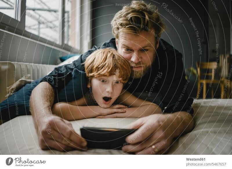 Portrait of father and son lying on couch looking at cell phone human human being human beings humans person persons caucasian appearance caucasian ethnicity
