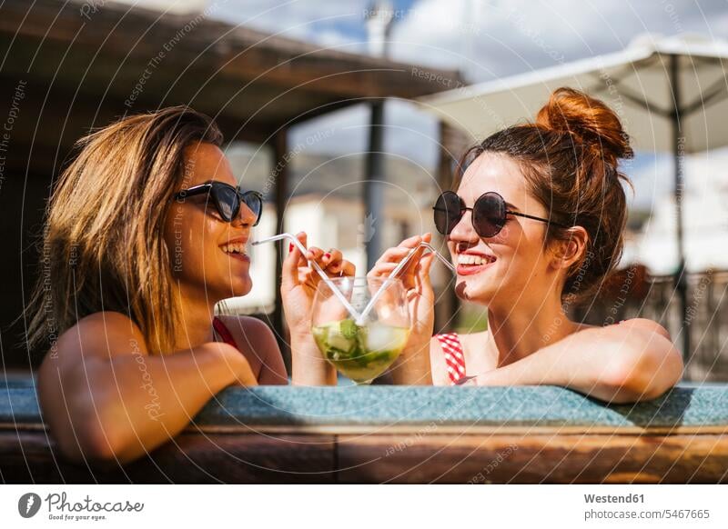 Two women having a drink in a jacuzzi friends mate female friend Drinking Glass Drinking Glasses drinking straw drinking straws swim wear bikinis Eye Glasses
