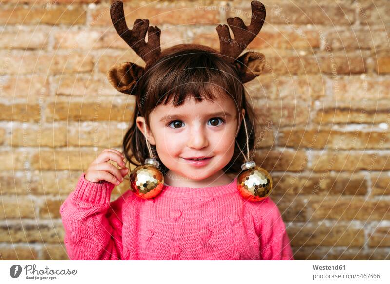 Portrait of smiling toddler girl wearing reindeer antlers headband and Christmas baubles Spain christmas bauble Christmas tree ball Christmas Ball Bauble
