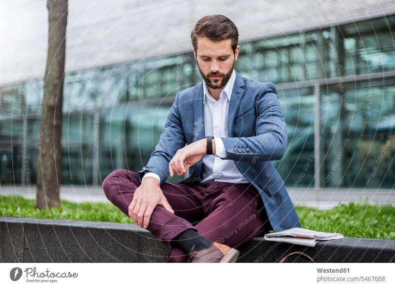 Young businessman sitting outdoors checking the time Time wrist watch Wristwatch Wristwatches wrist watches Businessman Business man Businessmen Business men