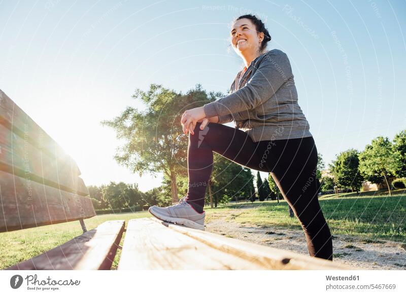 Female jogger stretching her leg on bench in park benches smile delight enjoyment Pleasant pleasure happy content Contented Emotion pleased free time