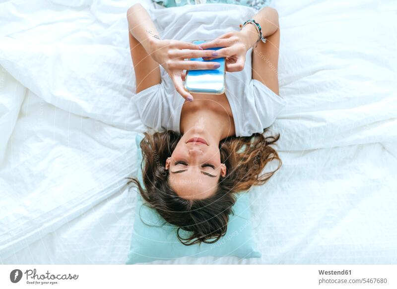 Top view of young woman lying in bed using cell phone human human being human beings humans person persons caucasian appearance caucasian ethnicity european 1