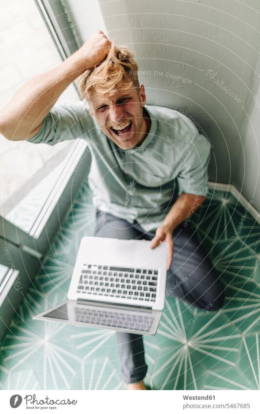 Young man sitting on ground, holding laptop, screaming in despair entrepreneur entrepreneurs enterpriser shouting anger Furious Wrath rage angry despaired